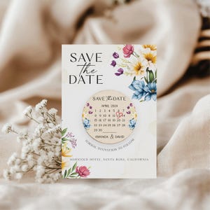 Puede incluir: Tarjeta de guardar la fecha con un dise&ntilde;o floral y un c&iacute;rculo de madera con un calendario para abril de 2024. La fecha 13 est&aacute; resaltada con un coraz&oacute;n rojo. El texto dice "Save the Date, abril de 2024, Amanda & David, Invitaci&oacute;n formal a seguir, Marigold Hotel, Santa Rosa, California."