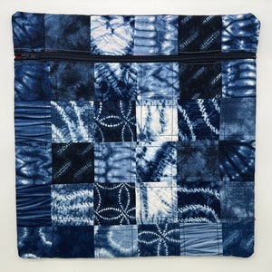 May include: A blue and white patchwork zippered pouch with a quilted design. The pouch is made of fabric squares with different tie-dye patterns.