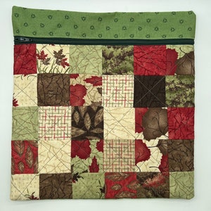 May include: A green and brown patchwork fabric zippered pouch with a quilted design. The pouch features a variety of leaf and floral patterns.