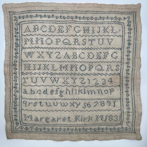 May include: A sampler with the alphabet, numbers, and the name "Margaret Kirk" embroidered in black thread on a beige linen background.