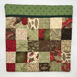 May include: A green zippered pouch with a patchwork design featuring various shades of green, brown, and red. The patchwork design includes leaves, branches, and geometric patterns.