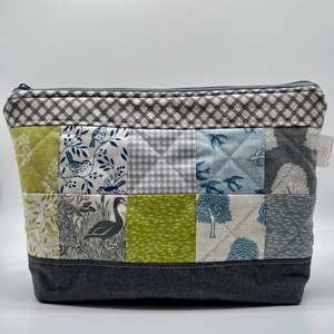 May include: A quilted zippered pouch with a patchwork design featuring various shades of blue, green, and grey. The pouch has a grey zipper and a grey fabric bottom.