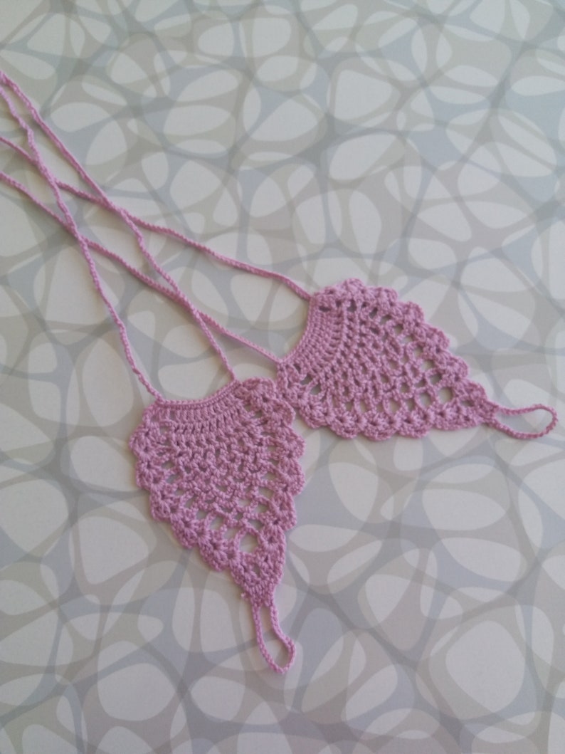 May include: A pair of crocheted foot jewelry in a light purple color. The jewelry is made of delicate crocheted lace and has a dangling design.