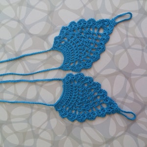 May include: A pair of blue crocheted foot jewelry with a delicate design. The jewelry is made of thin yarn and has a simple, elegant look.