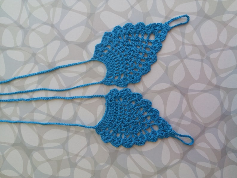 May include: A pair of blue crocheted foot jewelry with a delicate design. The jewelry is made of thin yarn and has a simple, elegant look.