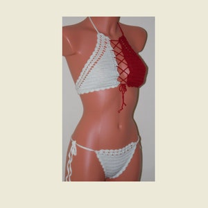 May include: A handmade crochet bikini set. The top is a halter style with a white left cup and a red right cup, laced together in the center. The matching bottoms are white, with tie sides. The set is displayed on a mannequin.