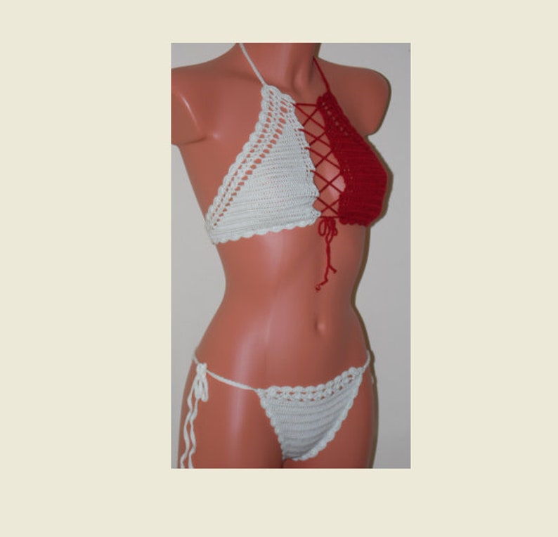 May include: A handmade crochet bikini set. The top is a halter style with a white left cup and a red right cup, laced together in the center. The matching bottoms are white, with tie sides. The set is displayed on a mannequin.