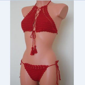 May include: A red crochet bikini set. The halter top features a lace-up design and tassels. The bottoms are a matching style with tie sides. The set is displayed on a mannequin.