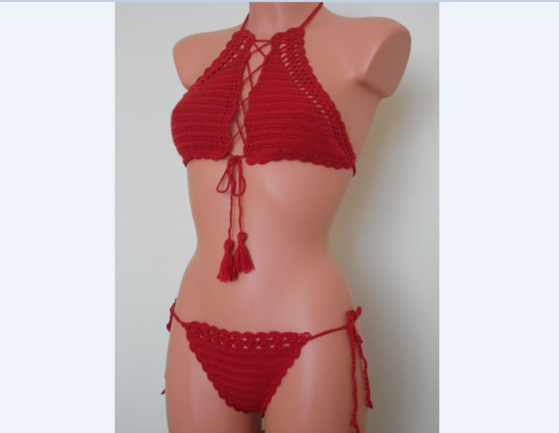 May include: A red crochet bikini set. The halter top features a lace-up design and tassels. The bottoms are a matching style with tie sides. The set is displayed on a mannequin.