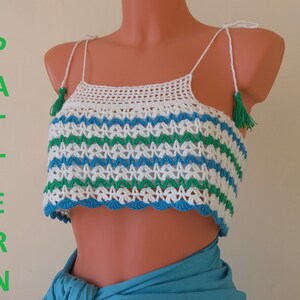 Pode incluir: Top branco de crochê com listras verdes e azuis e borlas nas alças. O top é de estilo cropped e tem uma bainha festonada.