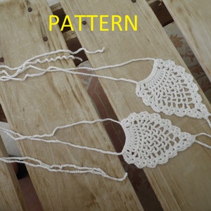 May include: Two white crocheted foot jewelry pieces with a delicate pattern. The jewelry is laid out on a wooden surface with the word "PATTERN" written in yellow letters above the jewelry.