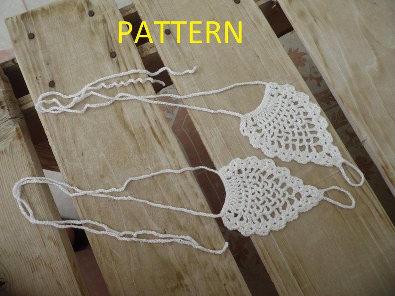 May include: Two white crocheted foot jewelry pieces with a delicate pattern. The jewelry is laid out on a wooden surface with the word "PATTERN" written in yellow letters above the jewelry.