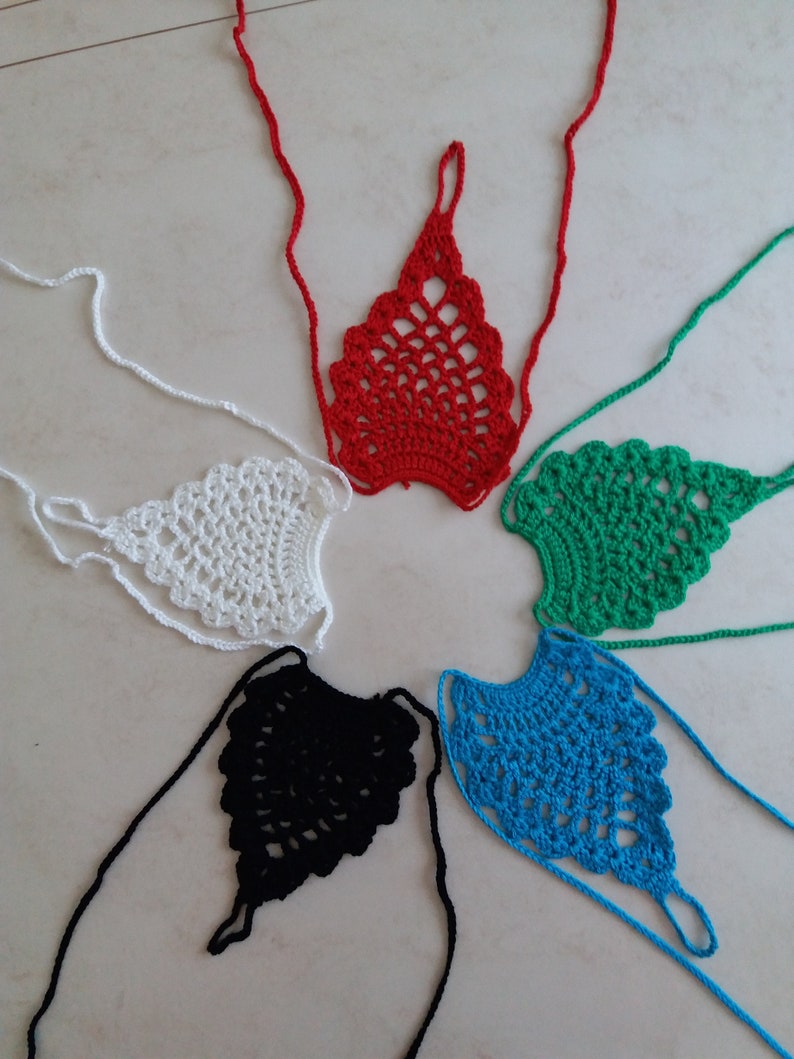 May include: Five crocheted foot covers in different colors: red, white, green, black, and blue. Each foot cover has a delicate, lacy design and is tied with long strings.