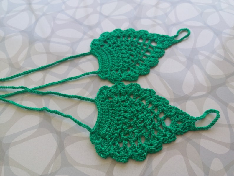 May include: A pair of green crocheted foot jewelry with a delicate design. The jewelry is made of a soft, lightweight yarn and is perfect for adding a touch of bohemian style to any outfit.