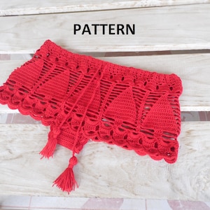 May include: A vibrant red, crocheted garment with a scalloped edge and tassel accents. The piece features a geometric openwork design and is displayed on a light-colored wooden surface. The word "PATTERN" is visible in the image.