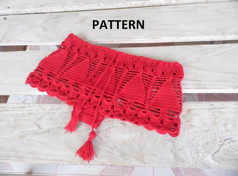 May include: A vibrant red, crocheted garment with a scalloped edge and tassel accents. The piece features a geometric openwork design and is displayed on a light-colored wooden surface. The word "PATTERN" is visible in the image.