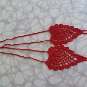 May include: A pair of red crocheted foot jewelry with long ties. The foot jewelry is made of a delicate, openwork pattern.