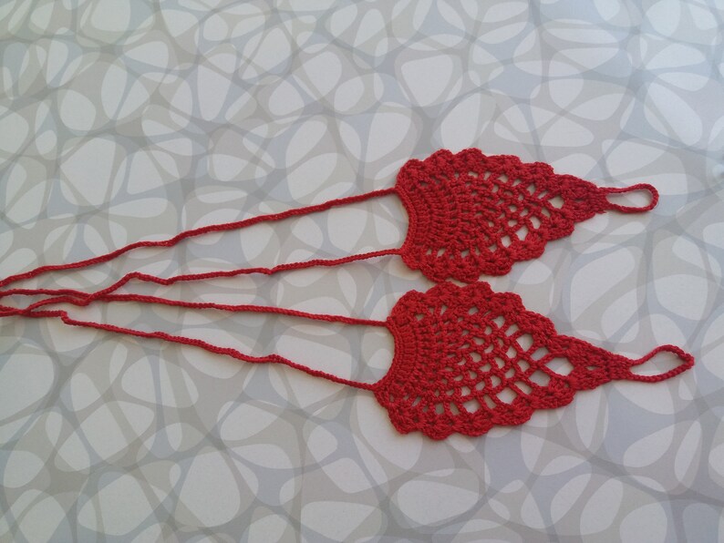 May include: A pair of red crocheted foot jewelry with long ties. The foot jewelry is made of a delicate, openwork pattern.
