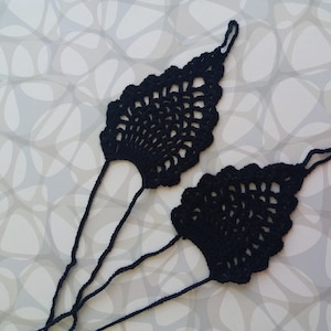 May include: A pair of black crocheted foot jewelry with a delicate, lacy design. The jewelry is made of thin yarn and has a long, flowing shape.