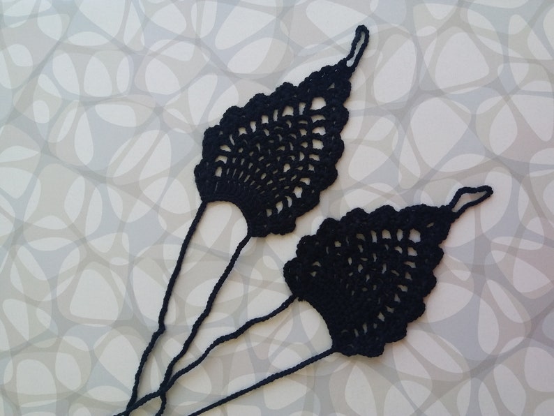 May include: A pair of black crocheted foot jewelry with a delicate, lacy design. The jewelry is made of thin yarn and has a long, flowing shape.