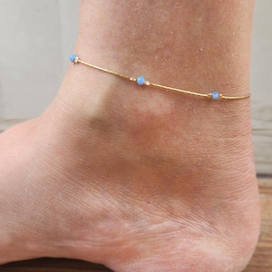 May include: A delicate gold anklet with small blue opal beads. The anklet is thin and dainty, perfect for layering with other jewelry.