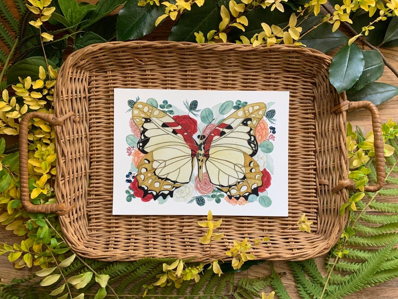 May include: A watercolour illustration of a butterfly with brown and white wings surrounded by pink, red and white flowers. The illustration is printed on white paper and framed in a wicker tray.