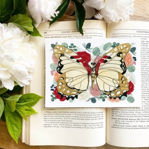 May include: A watercolour painting of a butterfly with red, white, and gold wings. The butterfly is surrounded by flowers and leaves in shades of pink, red, and green. The image is from a book about entomology.