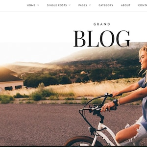 May include: A woman smiles as she rides a white bicycle down a paved road. The road is lined with tall grass and trees. The sun is setting in the background, casting a warm glow over the scene. The text "GRAND BLOG" is displayed at the top of the image.