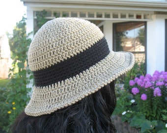 May include: A crocheted sun hat with a wide brim and a black band around the crown. The hat is made of a beige yarn and has a textured pattern.