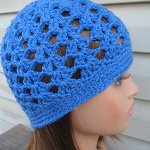 Peut inclure: Un bonnet bleu en crochet avec un motif ajour&eacute;. Le bonnet est port&eacute; sur un mannequin aux cheveux longs et bruns.