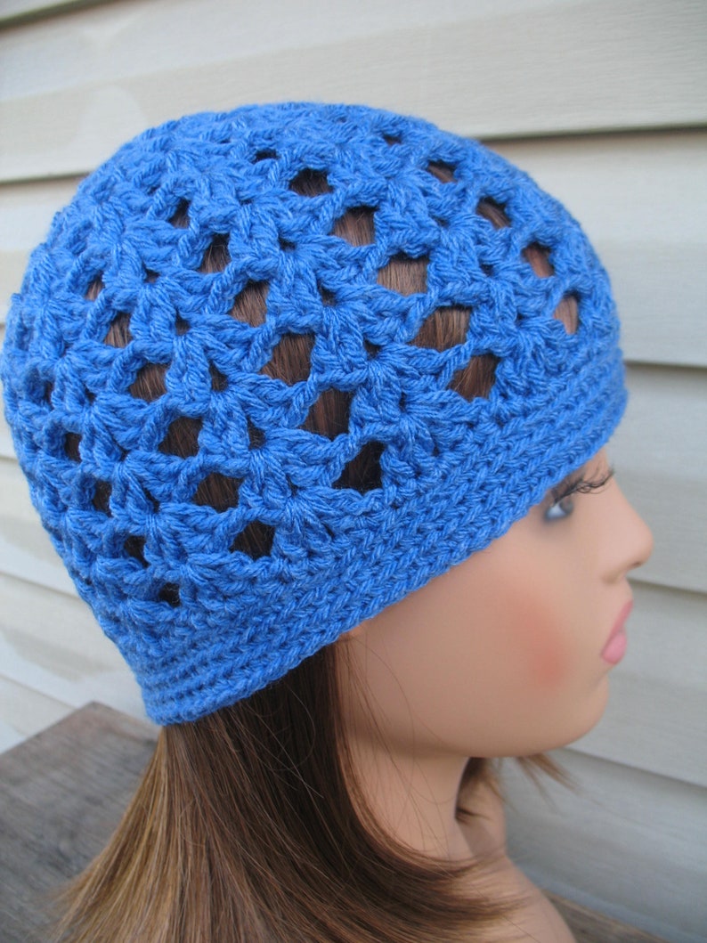 Peut inclure: Un bonnet bleu en crochet avec un motif ajour&eacute;. Le bonnet est port&eacute; sur un mannequin aux cheveux longs et bruns.