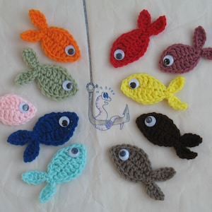 May include: Nine crocheted fish with googly eyes in various colors, including pink, blue, green, orange, red, yellow, brown, and gray. The fish are arranged in a circle around a hook and worm.