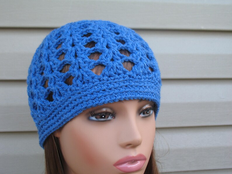 Peut inclure: Un bonnet bleu en crochet avec un motif ajour&eacute;. Le bonnet est sur une t&ecirc;te de mannequin.