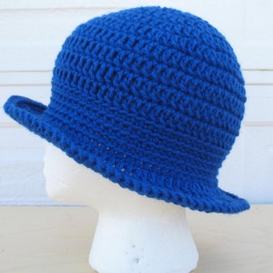 Puede incluir: Un sombrero azul de ganchillo con un ala ancha. El sombrero está hecho con un patrón de punto simple y tiene un estilo clásico y atemporal.
