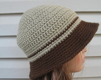 May include: A crocheted hat with a brown brim and a beige crown. The hat is made with a simple stitch pattern and has a wide brim.