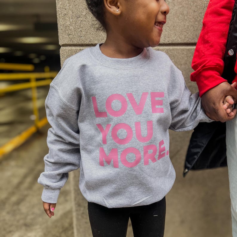 May include: A gray sweatshirt with the words "LOVE YOU MORE" printed in pink on the front.