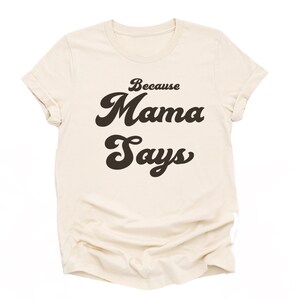 May include: A beige t-shirt with the text "Because Mama Says" in a retro font.