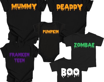 May include: A collection of black short-sleeved shirts and a baby bodysuit featuring dripping text. The shirts display the words MUMMY, DEADDY, ZOMBAE, FRANKEN TEEN, and BOO in orange, green, purple, and white, while the bodysuit says PUMPKIN.