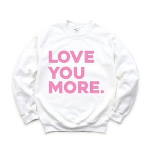 May include: White sweatshirt with the phrase "LOVE YOU MORE" printed in pink.