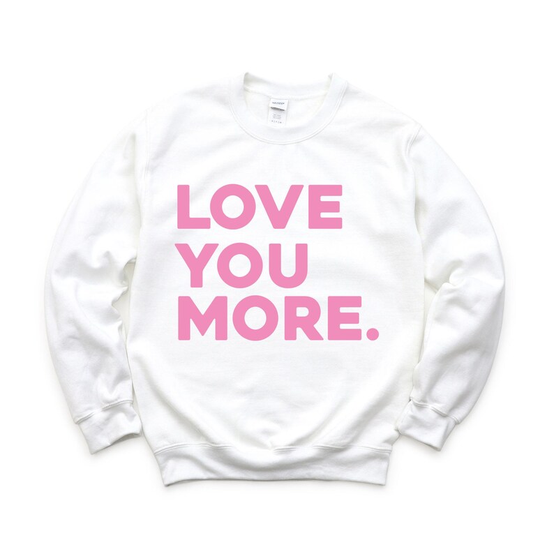 May include: White sweatshirt with the phrase "LOVE YOU MORE" printed in pink.
