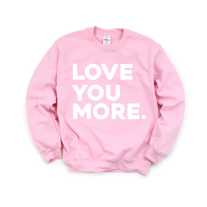 May include: Pink sweatshirt with the text "LOVE YOU MORE." printed in white.