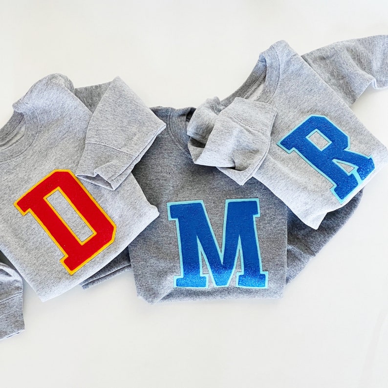 May include: Three gray sweatshirts with large felt letters. The letters are red, blue, and blue. The letters spell out "DMR".