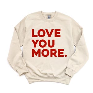 May include: A cream colored sweatshirt with the words "LOVE YOU MORE." printed in red.