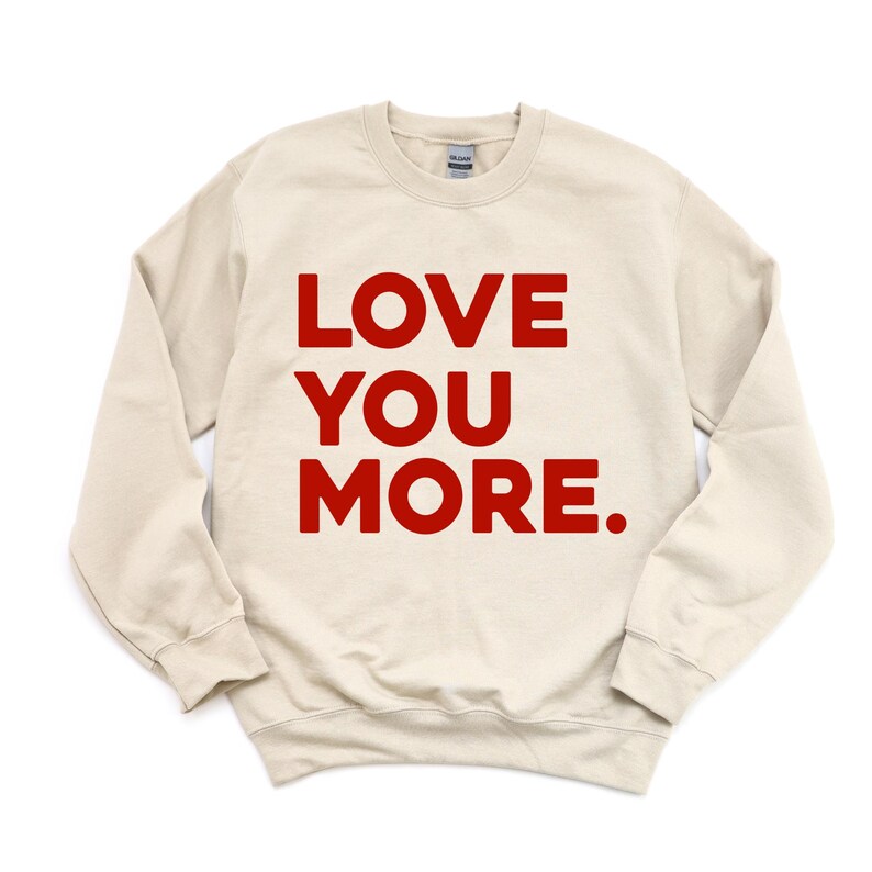 May include: A cream colored sweatshirt with the words "LOVE YOU MORE." printed in red.
