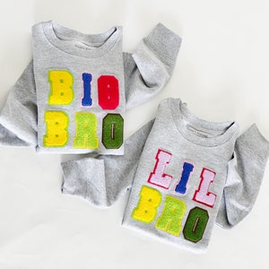 May include: Two grey sweatshirts with colourful felt letters spelling "Big Bro" and "Lil Bro".