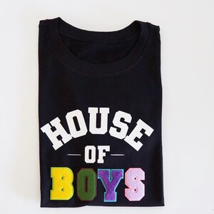 May include: Black t-shirt with white text that reads "HOUSE OF BOYS". The word "BOYS" is in colorful letters.