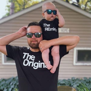 May include: A father and son wearing matching black t-shirts with white text. The father's shirt says "The Original" and the son's shirt says "The Remix." Both are wearing sunglasses.