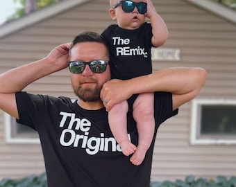 Może przedstawiać: Ojciec i syn w dopasowanych czarnych koszulkach z białym nadrukiem. Koszulka ojca ma napis "The Original", a koszulka syna "The Remix". Oboje noszą okulary przeciwsłoneczne.
