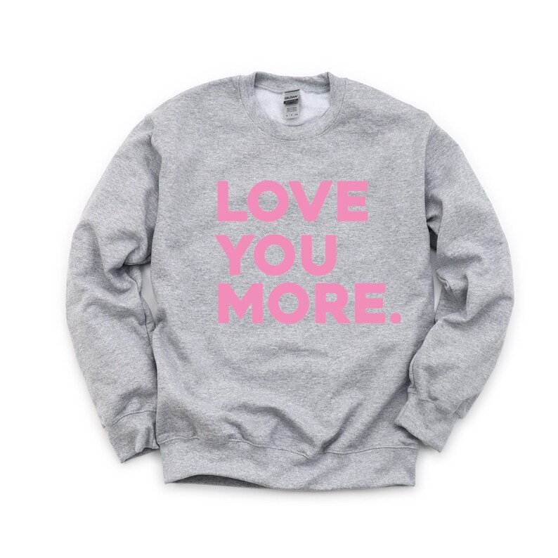 May include: A gray sweatshirt with the words "LOVE YOU MORE" printed in pink.