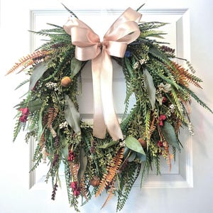 May include: A decorative wreath featuring a mix of green and rust-colored foliage, eucalyptus leaves, small white berries, and dark red floral accents. A large, smooth, light champagne-colored satin ribbon is tied in a bow at the top center.
